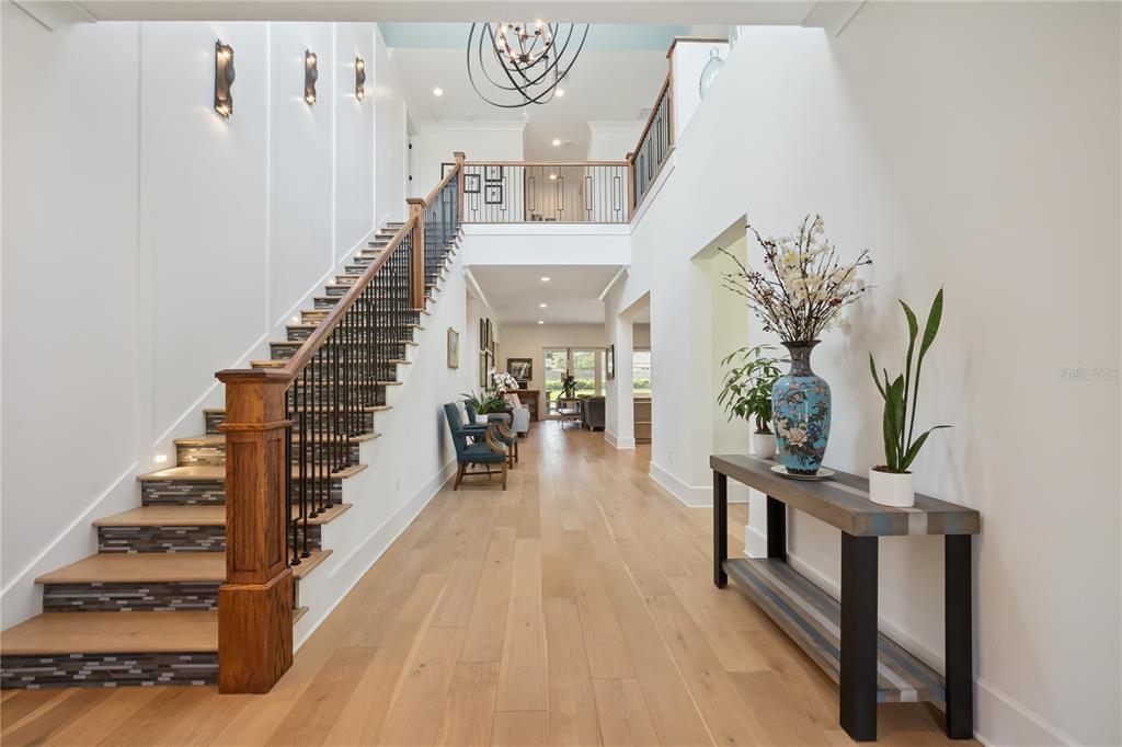 A bright foyer features light wood flooring, a staircase with iron railings, and a console table — 11539 LAKE BUTLER BOULEVARD, WINDERMERE, FL