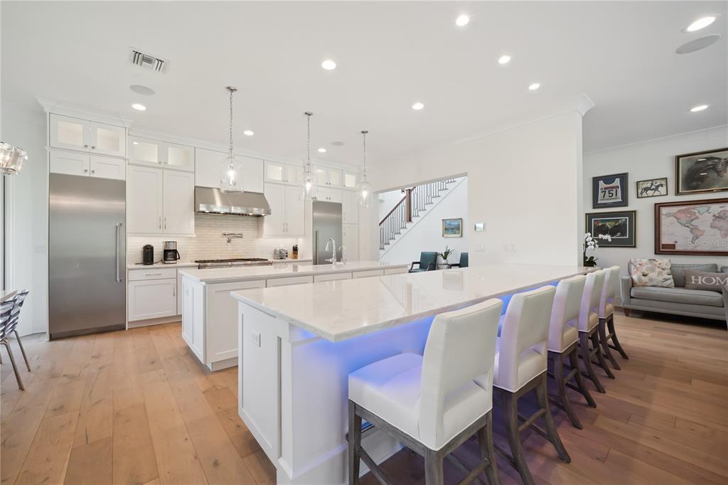 A white kitchen features a large island with bar seating, stainless appliances, and hardwood floors — 11539 LAKE BUTLER BOULEVARD, WINDERMERE, FL