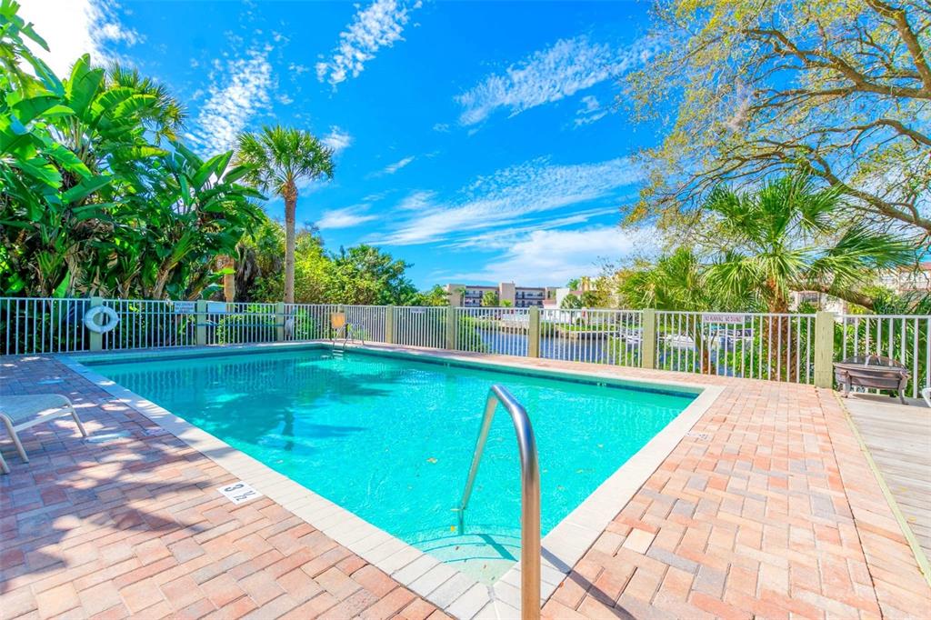 An outdoor swimming pool with a brick deck, white fence, and palm trees under blue sky — 5551 EXECUTIVE DRIVE, NEW PORT RICHEY, FL