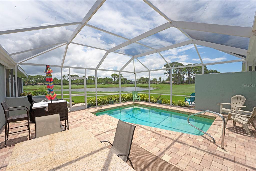 A screened-in patio features a small swimming pool, brick pavers, and views of a pond — 5903 W 43RD ST. W. UNIT 5903, BRADENTON, FL