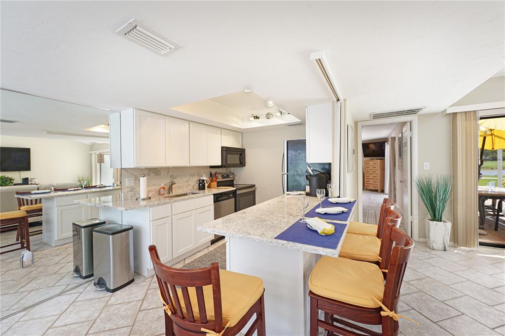 A kitchen features white cabinets, granite countertops, a central island, and tile flooring — 5903 W 43RD ST. W. UNIT 5903, BRADENTON, FL