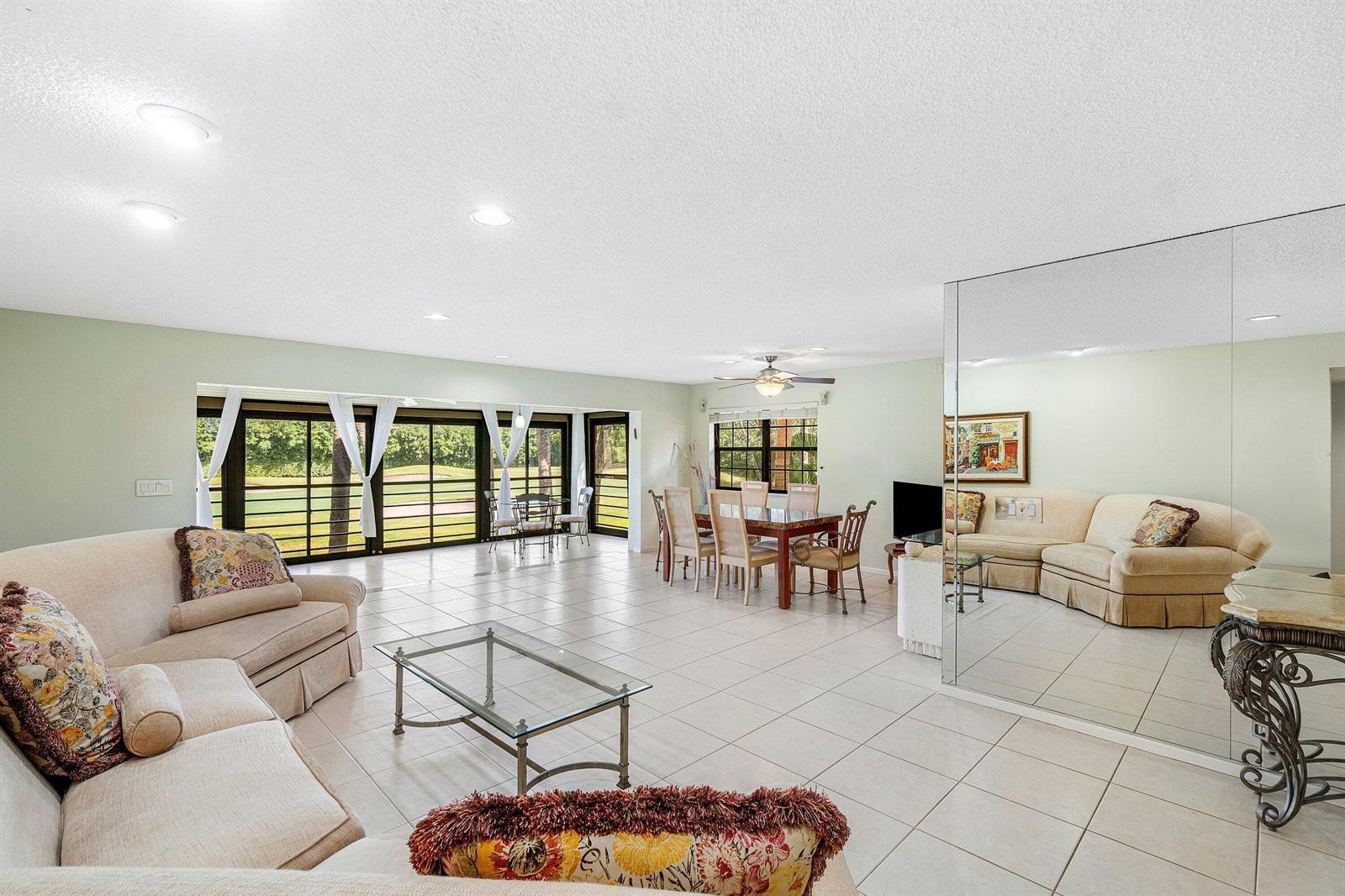 A spacious living and dining area with tile floors, mirrored walls, and large sliding glass doors — 6446 Aspen Glen Circle, Boynton Beach FL 33437, BOYNTON BEACH, FL