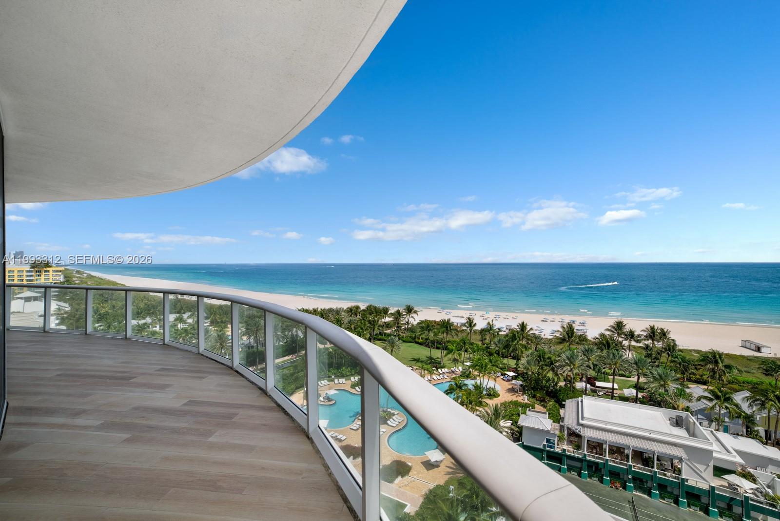A curved balcony with glass railings overlooks a beach, ocean, and swimming pool — 100 S Pointe Dr, Miami Beach FL 33139, MIAMI BEACH, FL