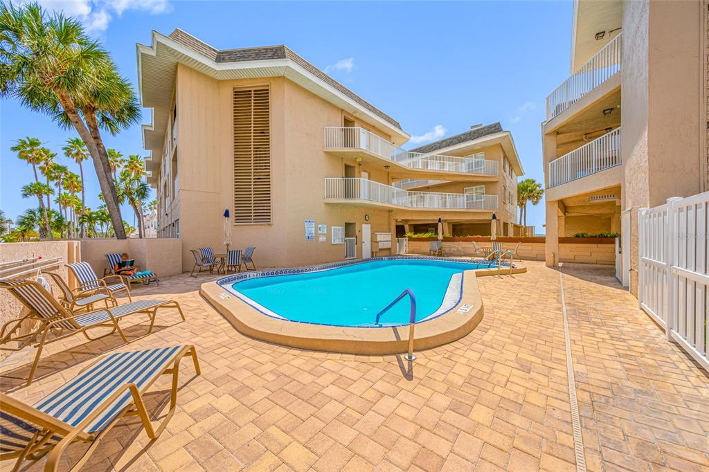 A swimming pool sits on a paved patio surrounded by multi-story tan apartment buildings — 3100 GULF BOULEVARD UNIT 132, BELLEAIR BEACH, FL