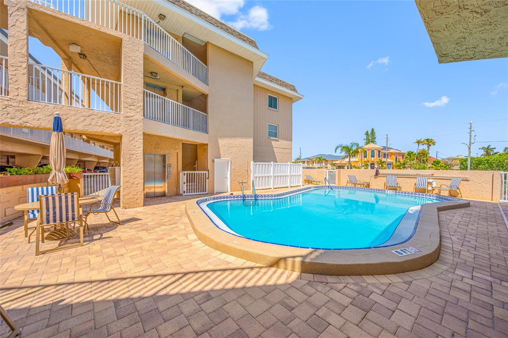 A swimming pool with a paved deck sits beside a multi-story building with balconies — 3100 GULF BOULEVARD UNIT 132, BELLEAIR BEACH, FL
