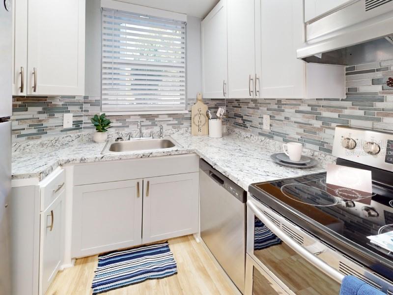 A kitchen features white cabinets, granite countertops, a stainless steel dishwasher, and a tiled backsplash — 4701 31ST STREET S UNIT B2, ST PETERSBURG, FL