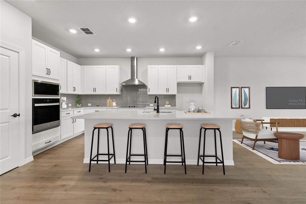 A modern kitchen features white cabinets, a large island with a sink, and stainless appliances — 614 KINGSWOOD COURT, BRADENTON, FL