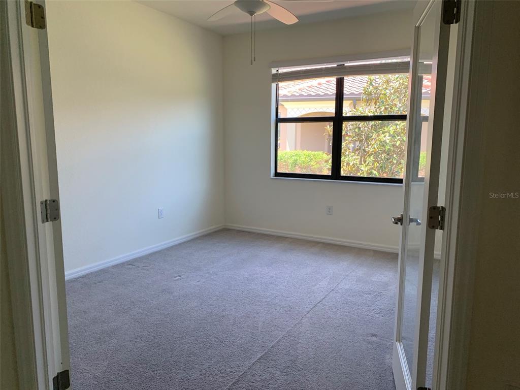 An empty room with beige carpet, white walls, a ceiling fan, and French doors — 12259 AMICA LOOP, VENICE, FL