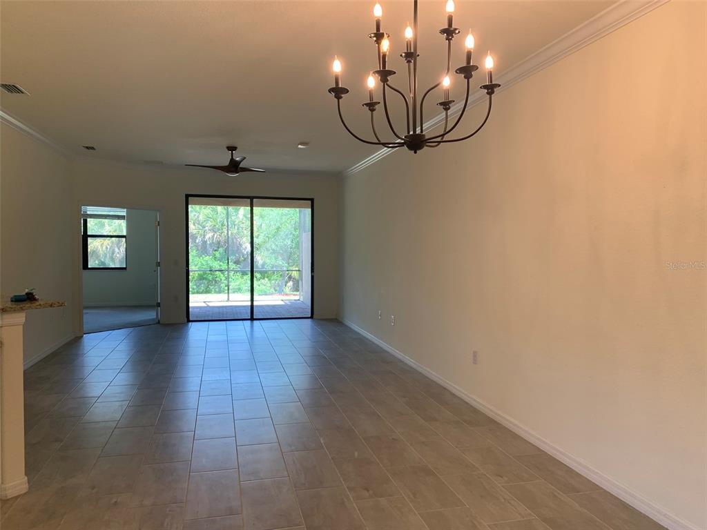 An open living area features tile flooring, a large chandelier, and sliding glass doors — 12259 AMICA LOOP, VENICE, FL