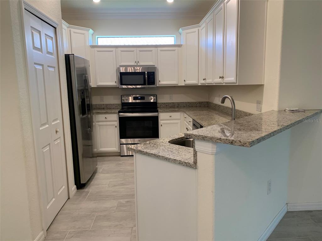 A kitchen features white cabinets, granite countertops, stainless steel appliances, and light-colored tile flooring — 12259 AMICA LOOP, VENICE, FL