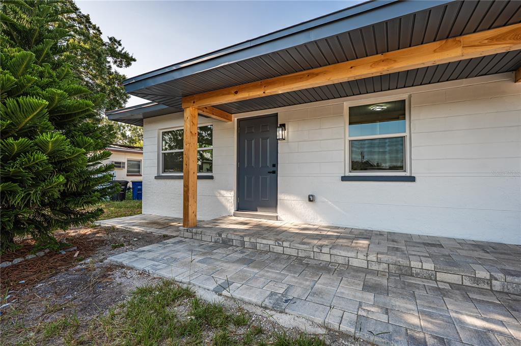 A white concrete block house features a gray front door and a paved stone porch — 1359 BARRY STREET, CLEARWATER, FL