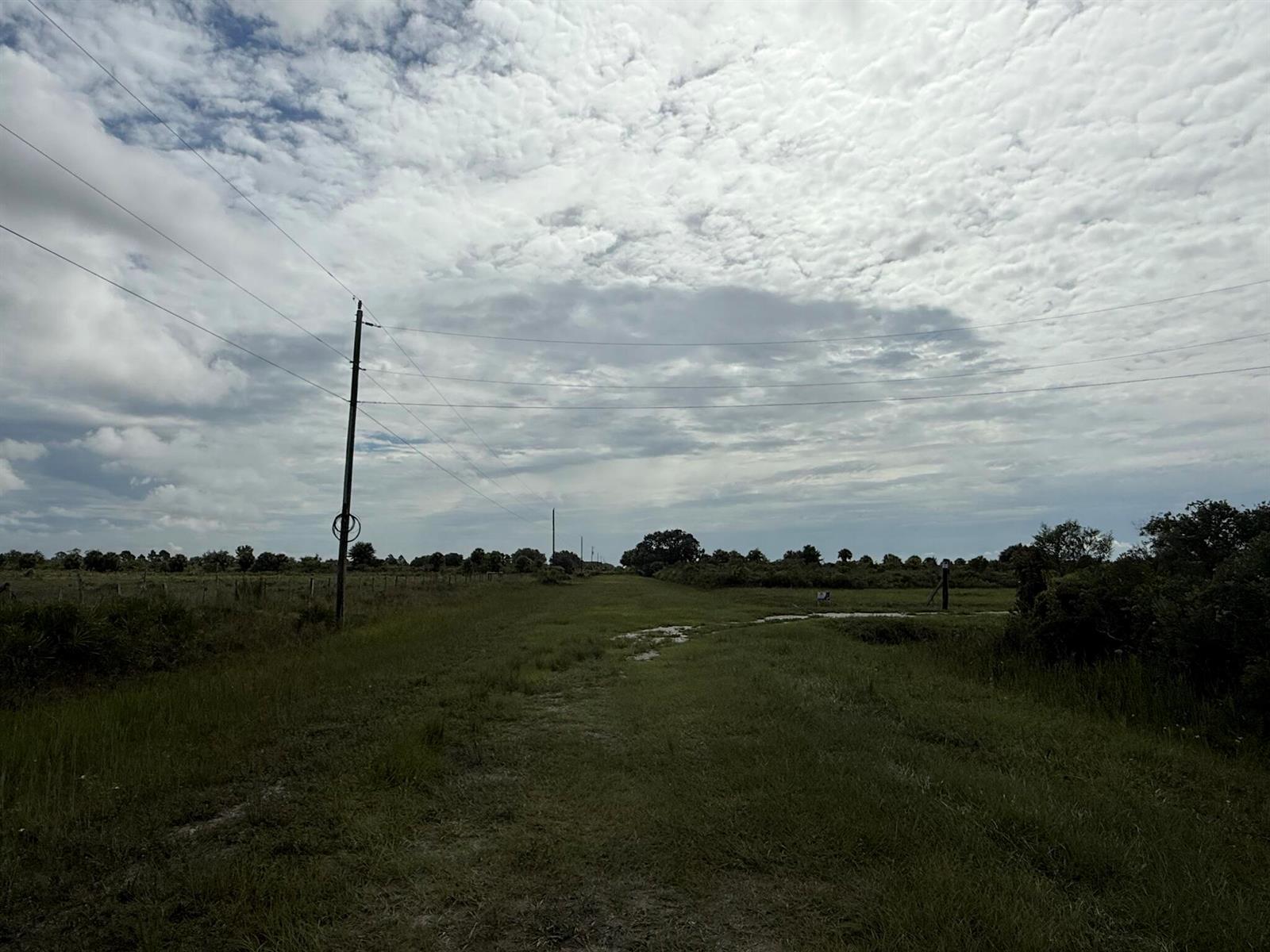A grassy path leads through an open field under a cloudy sky with utility poles — 18619 NW 248th Street, Okeechobee FL 34972, OKEECHOBEE, FL