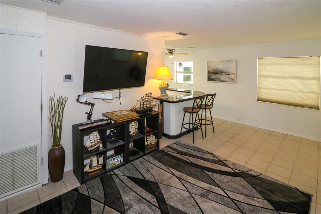 A living room features a wall-mounted television, a black shelving unit, and a breakfast bar — 3580 SWANEE ROAD, PORT CHARLOTTE, FL