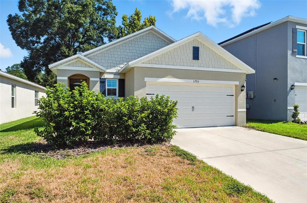 A single-story house with a white garage door, beige stucco walls, and a green bush — 1753 BENT BRANCH AVENUE, DELAND, FL