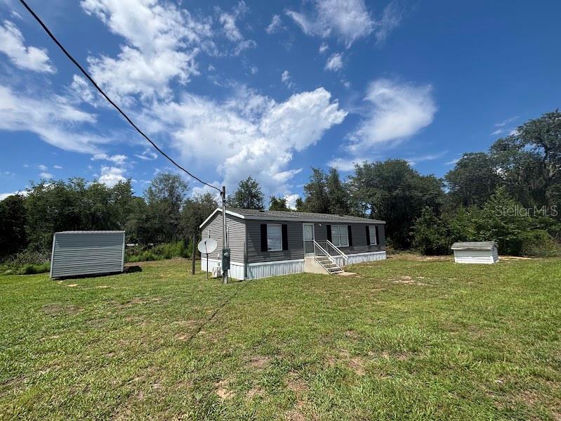A manufactured home sits on a grassy lot with two small sheds nearby — 15299 NE 238TH STREET, FORT MC COY, FL