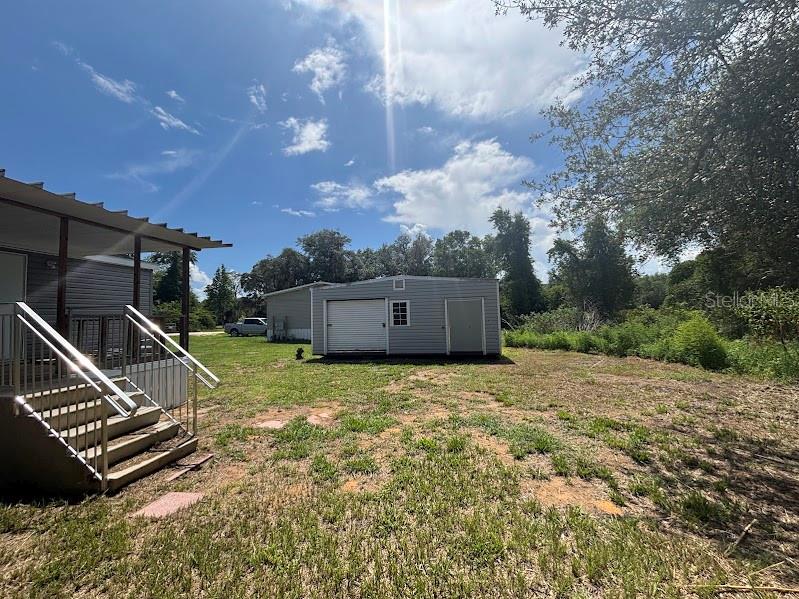 A detached garage and shed sit in a grassy yard next to a house porch — 15299 NE 238TH STREET, FORT MC COY, FL