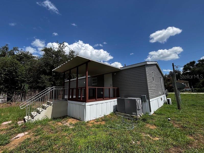 A mobile home features a covered wooden porch, metal stairs, and grey vinyl siding — 15299 NE 238TH STREET, FORT MC COY, FL