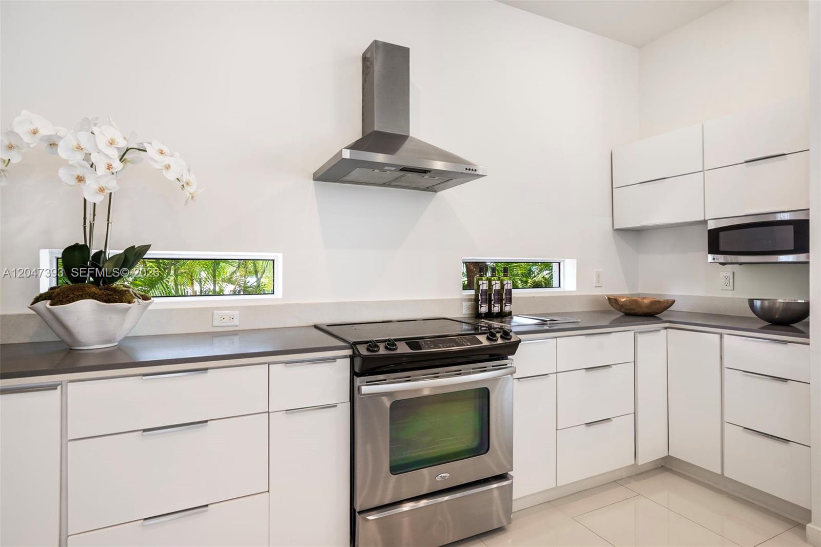 A modern kitchen features white flat-panel cabinets, stainless steel appliances, and horizontal windows — 3253 Mcdonald St, Miami FL 33133, MIAMI, FL