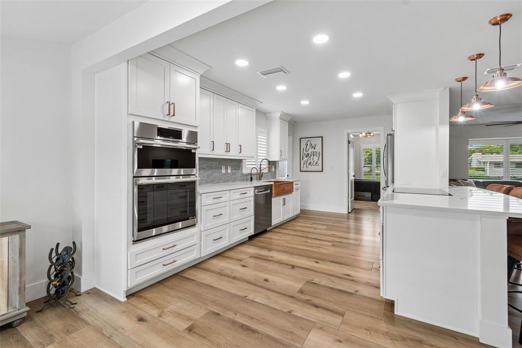 A modern kitchen features white cabinetry, stainless steel appliances, a copper sink, and wood flooring — 3941 E EDEN ROC CIRCLE, TAMPA, FL