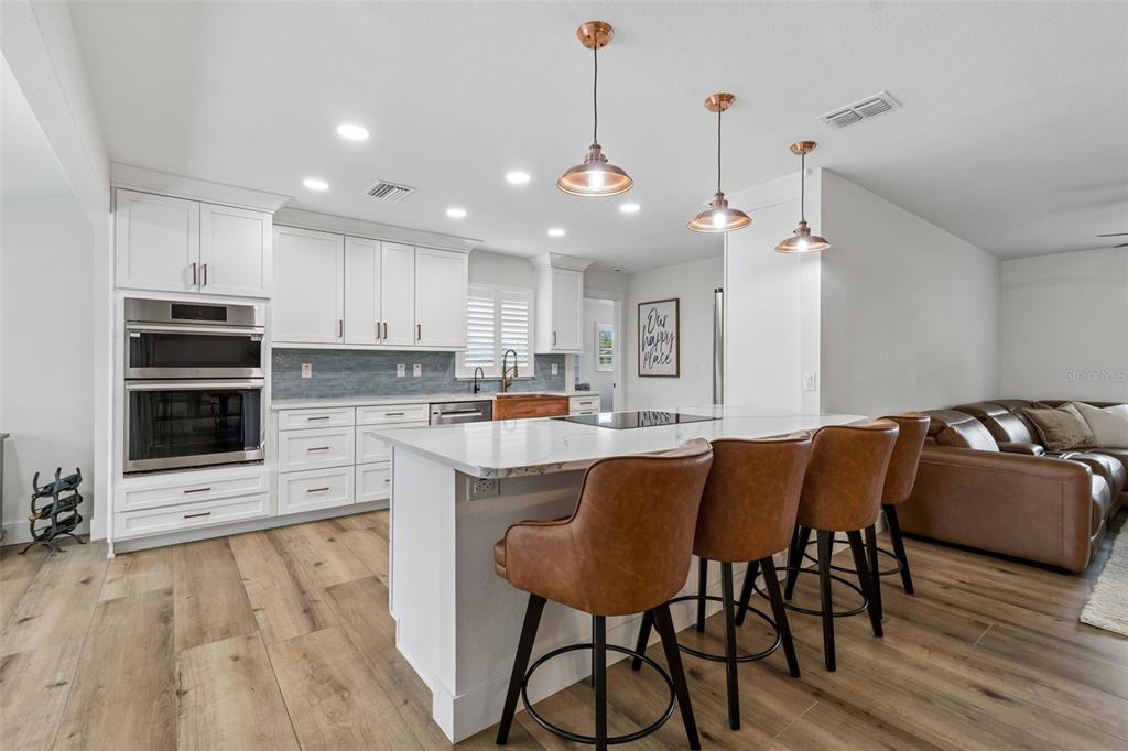 A modern kitchen features white cabinetry, a large island with bar stools, and wood flooring — 3941 E EDEN ROC CIRCLE, TAMPA, FL