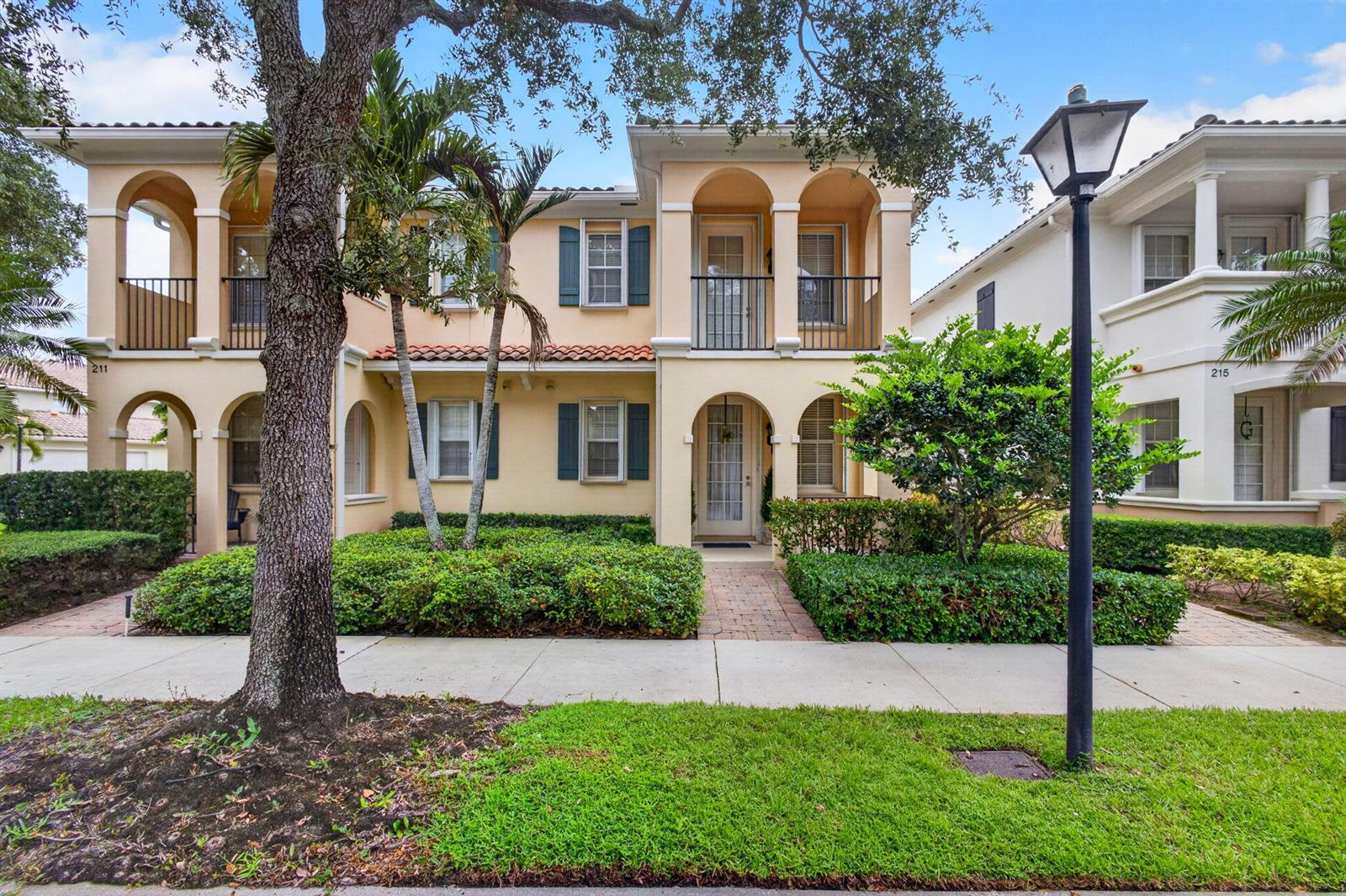 A two-story tan stucco townhouse with arched entryways, balconies, and a landscaped front yard — 213 Barcelona Drive, Jupiter FL 33458, JUPITER, FL