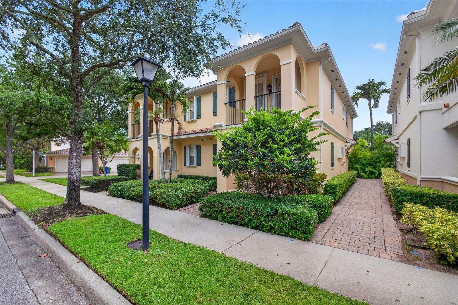 A two-story, yellow stucco townhouse with arched balconies, green shutters, and a brick walkway — 213 Barcelona Drive, Jupiter FL 33458, JUPITER, FL
