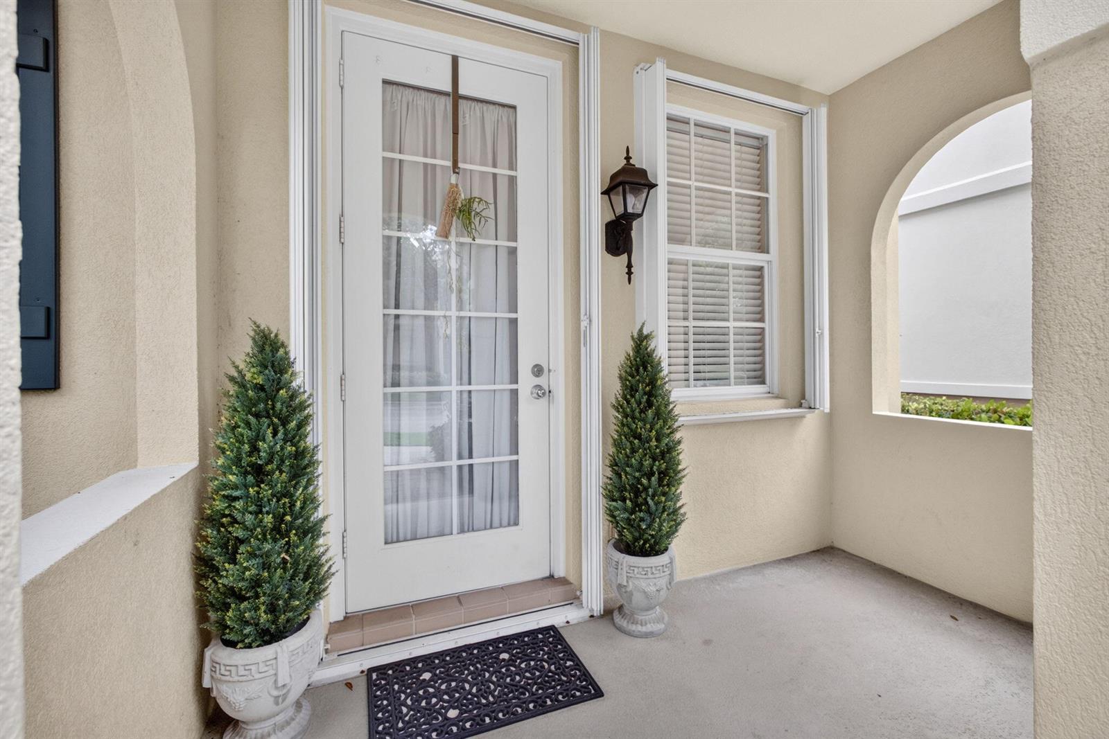 A covered entryway features a white glass-paneled door, a window with blinds, and two potted topiaries — 213 Barcelona Drive, Jupiter FL 33458, JUPITER, FL