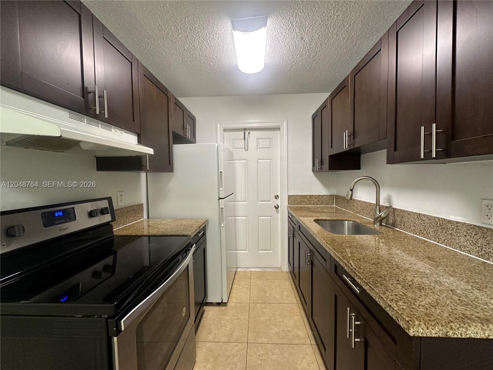 A galley kitchen features dark wood cabinets, granite countertops, and stainless steel appliances — 2900 NE 17th Ave # 109, Pompano Beach FL 33064, POMPANO BEACH, FL