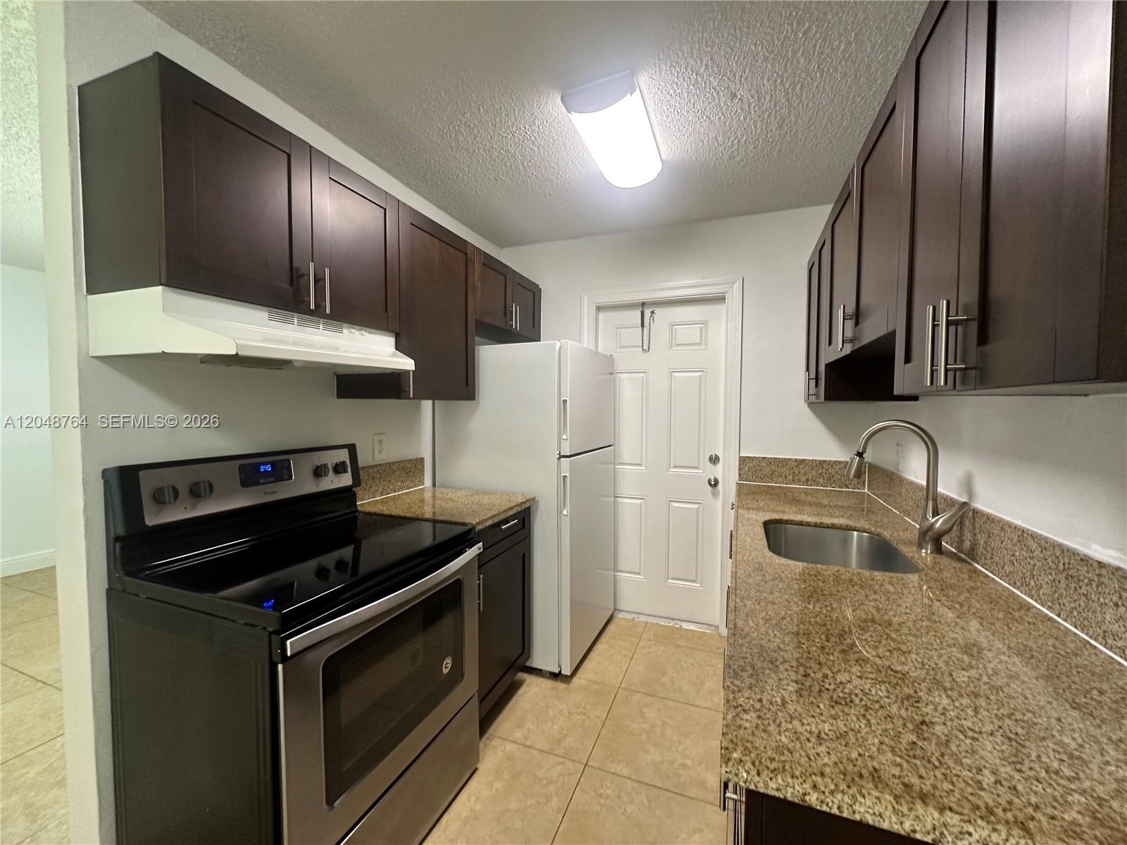 A galley kitchen features dark wood cabinets, granite countertops, and stainless steel appliances — 2900 NE 17th Ave # 109, Pompano Beach FL 33064, POMPANO BEACH, FL