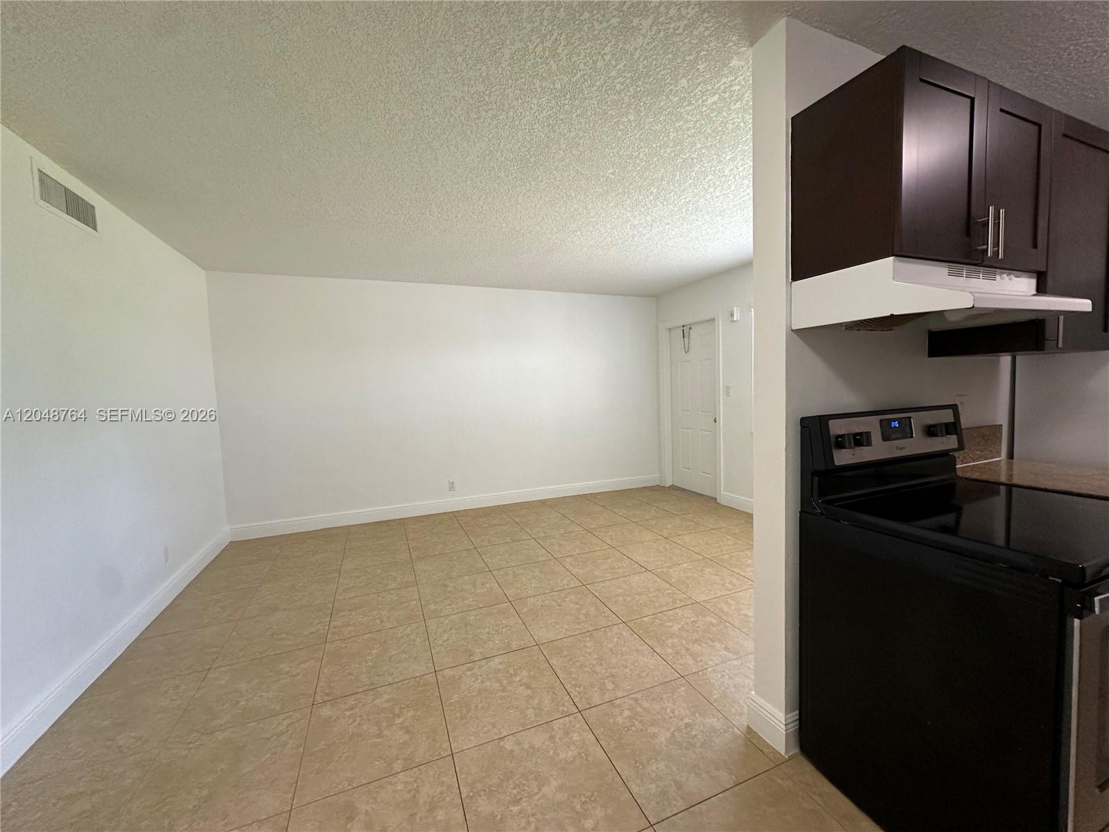 An open-concept room features beige tile flooring, white walls, and a partial kitchen view — 2900 NE 17th Ave # 109, Pompano Beach FL 33064, POMPANO BEACH, FL