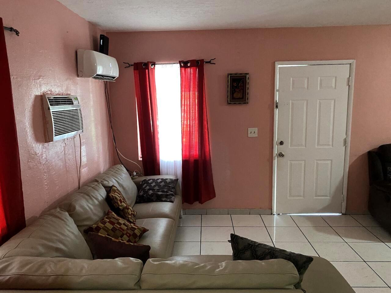 A living room with pink walls, a beige sectional sofa, tile floors, and a white door — 12920 Westview Drive # 1, Miami FL 33167, MIAMI, FL