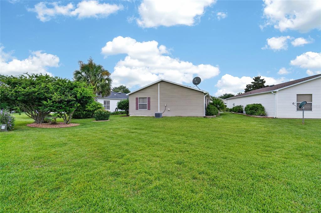 The exterior view shows the side of a tan house with a large grassy yard — 2673 SUFFOLK STREET, THE VILLAGES, FL