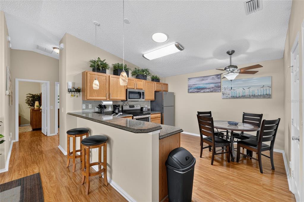 A kitchen with wood cabinets and a breakfast bar opens into a dining area — 2673 SUFFOLK STREET, THE VILLAGES, FL