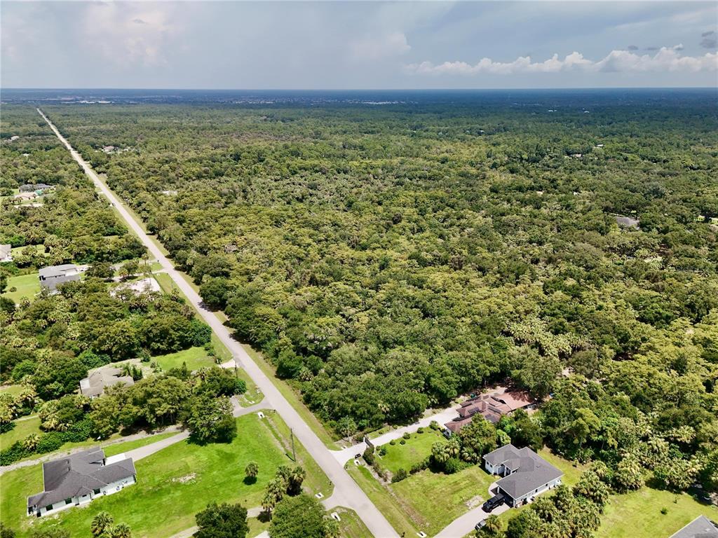 An aerial view shows a paved road running through a wooded area with scattered houses — 35TH AVENUE NW, NAPLES, FL