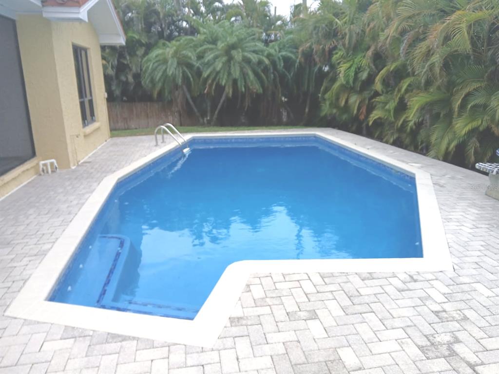 A rectangular swimming pool with a corner step area sits on a paved patio — 562 JOHNS PASS AVENUE, MADEIRA BEACH, FL
