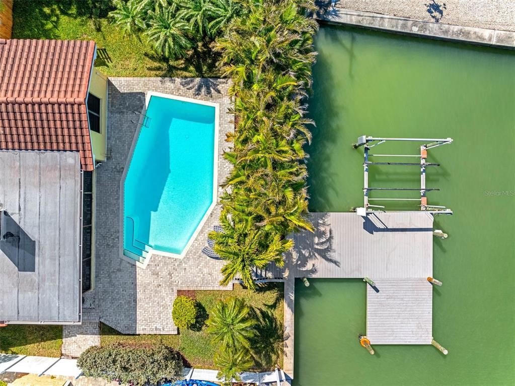 An aerial view shows a swimming pool, a wooden dock, and palm trees by water — 562 JOHNS PASS AVENUE, MADEIRA BEACH, FL