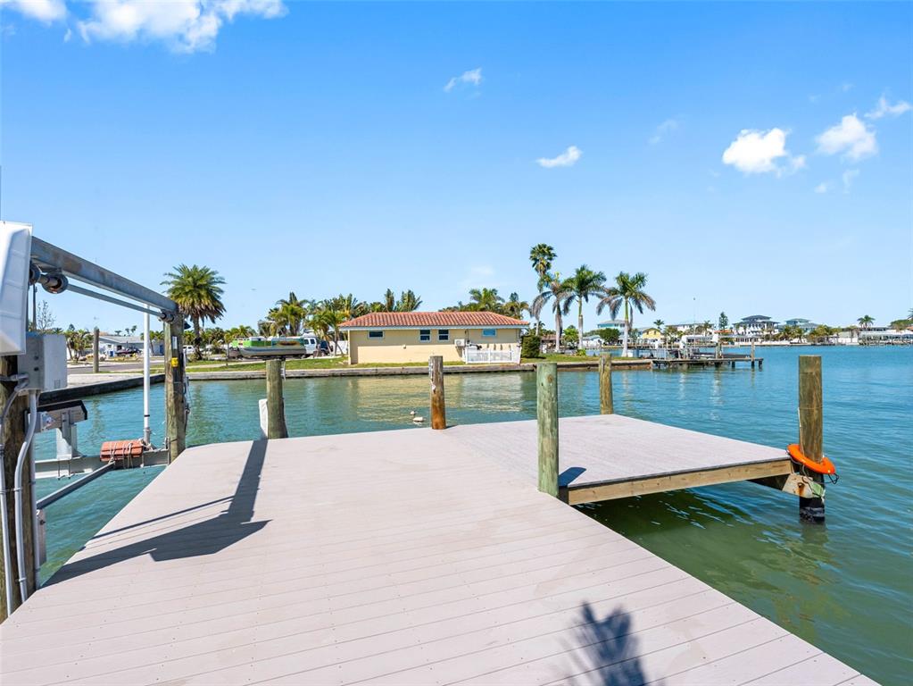 A wooden boat dock extends over calm water toward a house with palm trees — 562 JOHNS PASS AVENUE, MADEIRA BEACH, FL