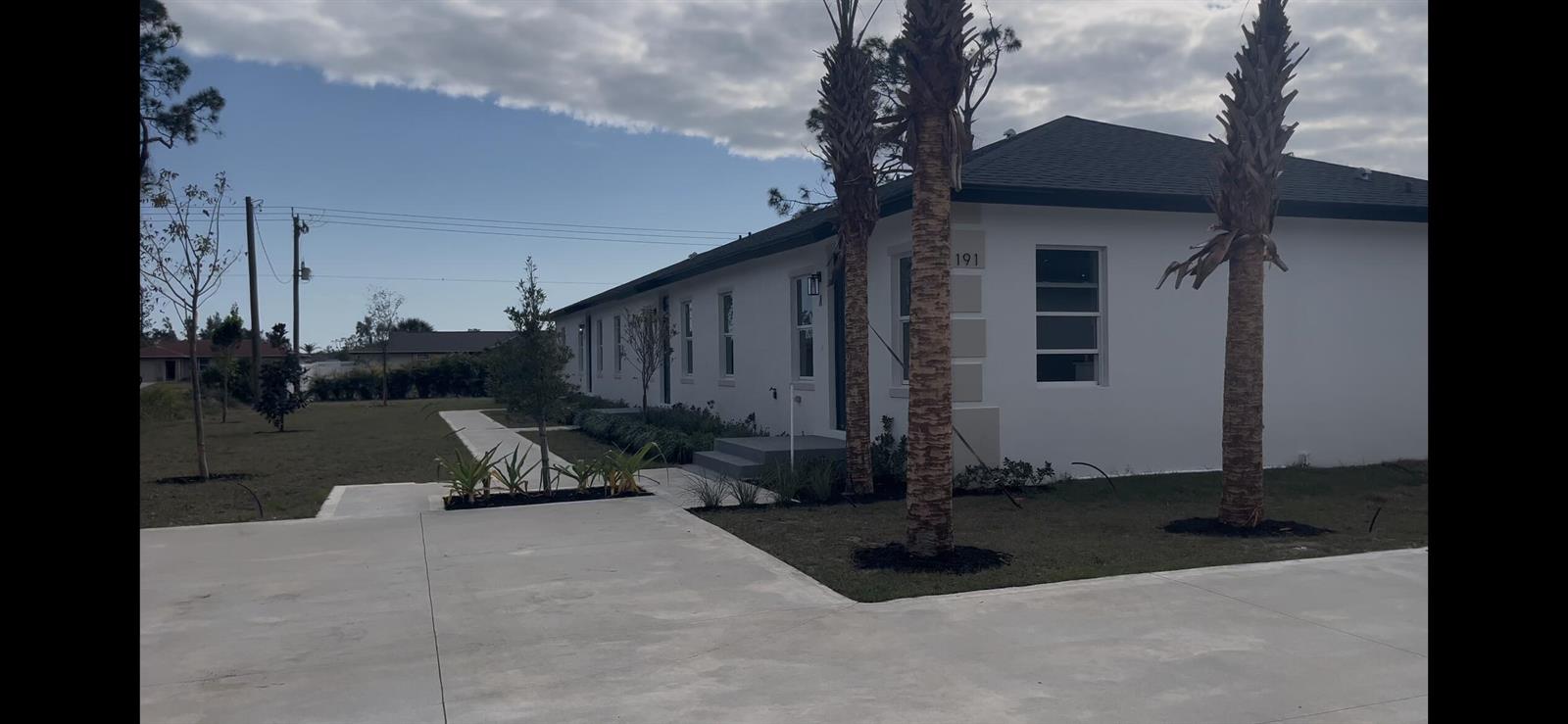 A white single-story building with a dark roof, palm trees, and a concrete driveway — 195 Rotonda Boulevard W Unit c, FL 33947, FL