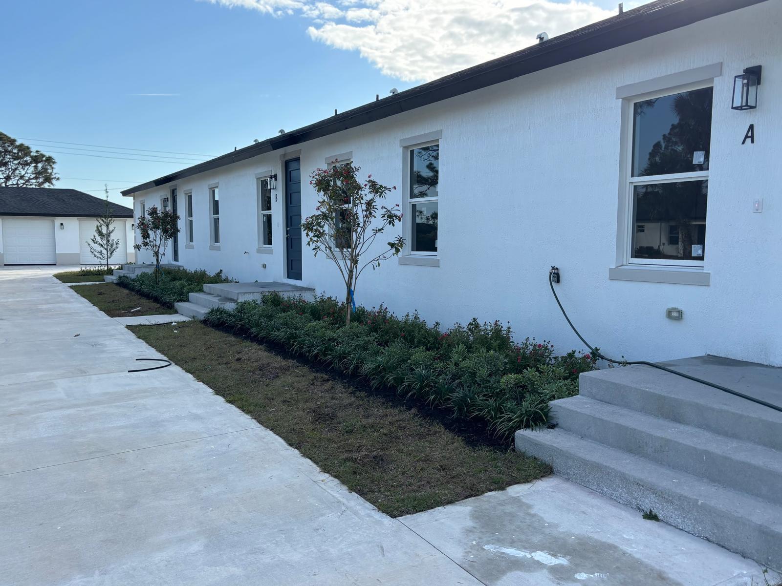 A white exterior of a multi-unit building with concrete steps, landscaping, and a paved driveway — 195 Rotonda Boulevard W Unit c, FL 33947, FL