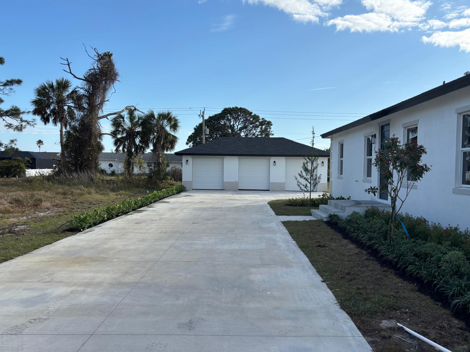 A white house with a three-car garage and a long concrete driveway under a blue sky — 195 Rotonda Boulevard W Unit c, FL 33947, FL