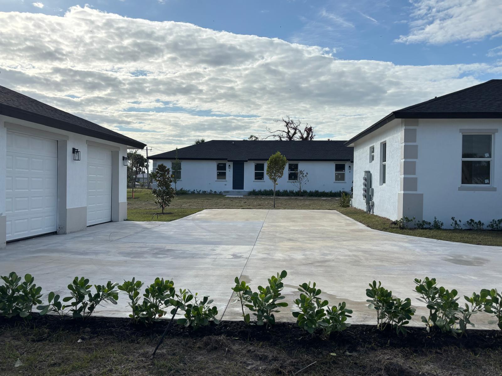 A concrete driveway sits between two white houses with dark roofs under a cloudy sky — 195 Rotonda Boulevard W Unit c, FL 33947, FL