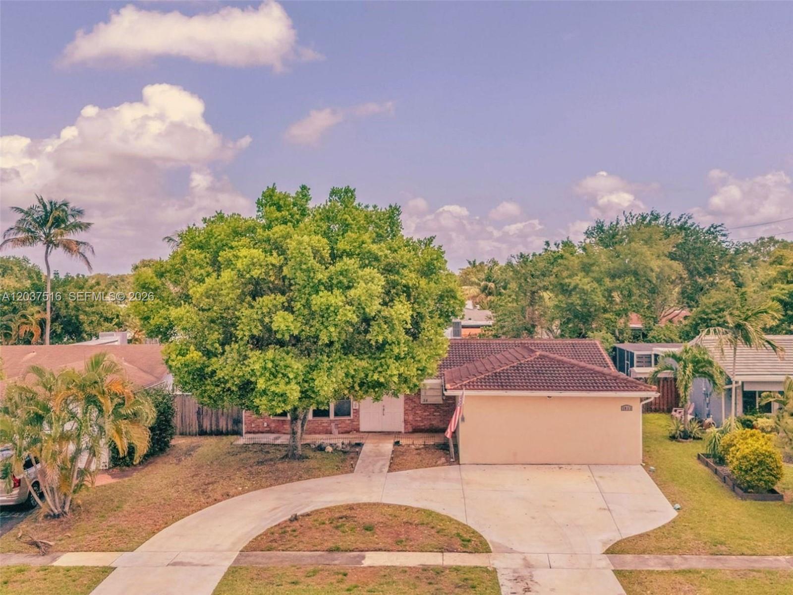 An exterior view of a single-story house with a large tree and concrete driveway — 1911 N 53rd Ave, Hollywood FL 33021, HOLLYWOOD, FL