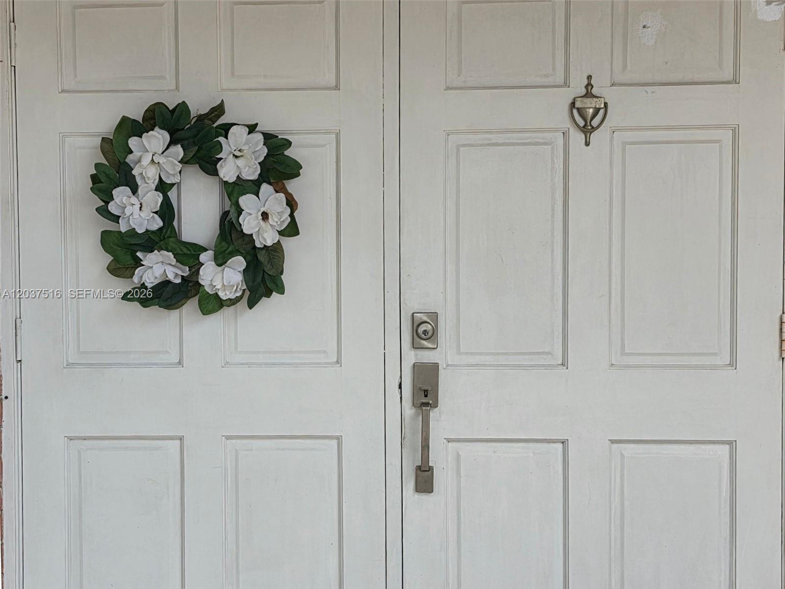 A white double door features a floral wreath, a door knocker, and metal hardware — 1911 N 53rd Ave, Hollywood FL 33021, HOLLYWOOD, FL