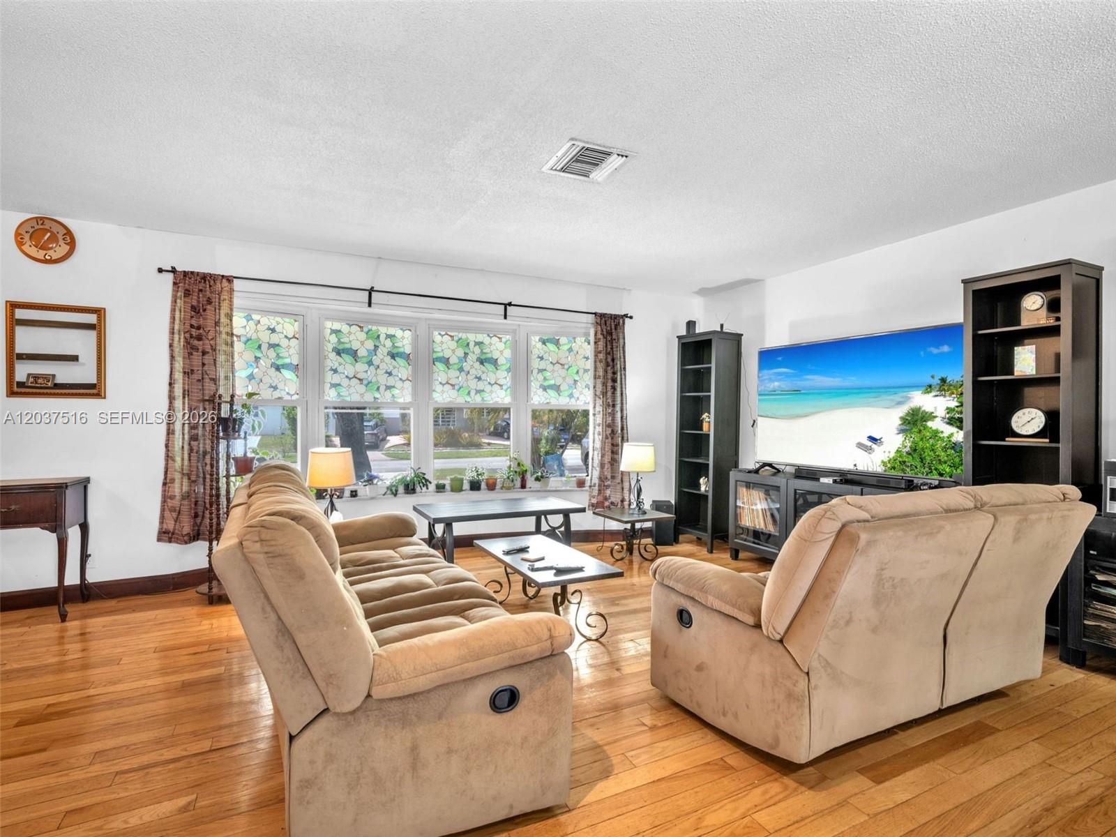 A living room features two beige reclining sofas, hardwood floors, and a large television — 1911 N 53rd Ave, Hollywood FL 33021, HOLLYWOOD, FL