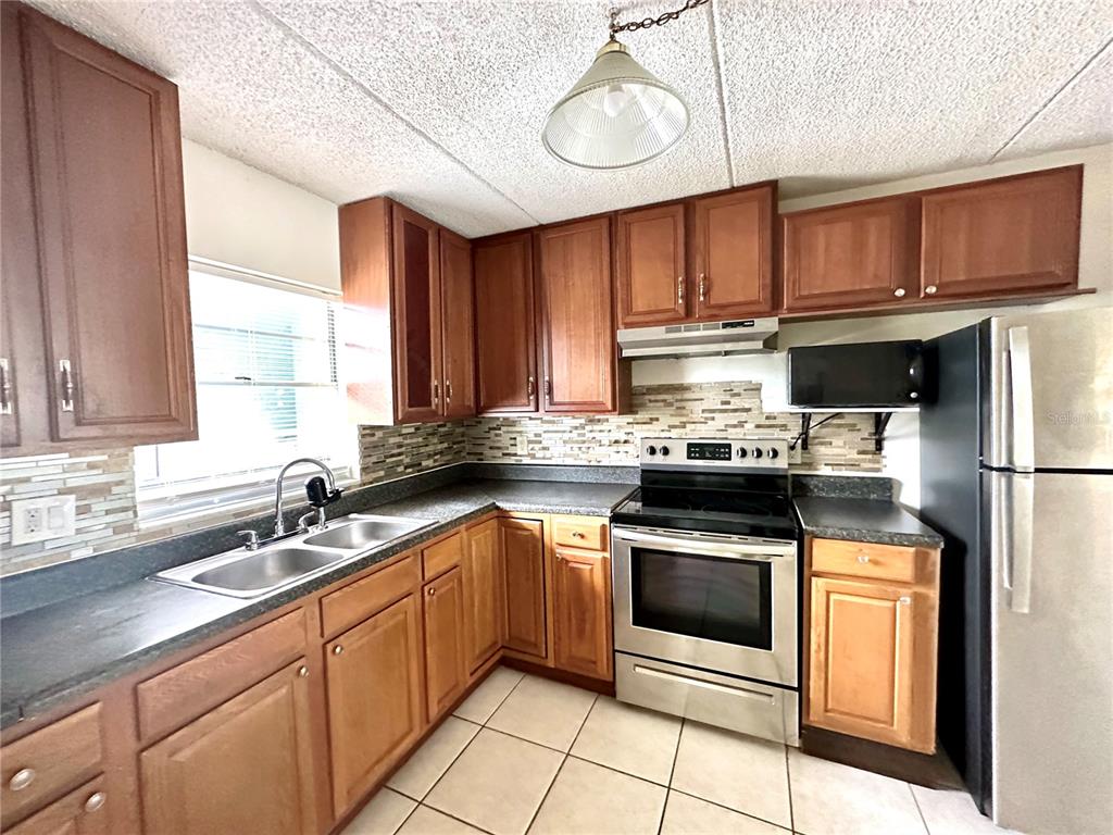 A kitchen with wood cabinets, stainless steel appliances, a tile backsplash, and light-colored floor tiles — 2830 SOMERSET PARK DRIVE UNIT 201, TAMPA, FL