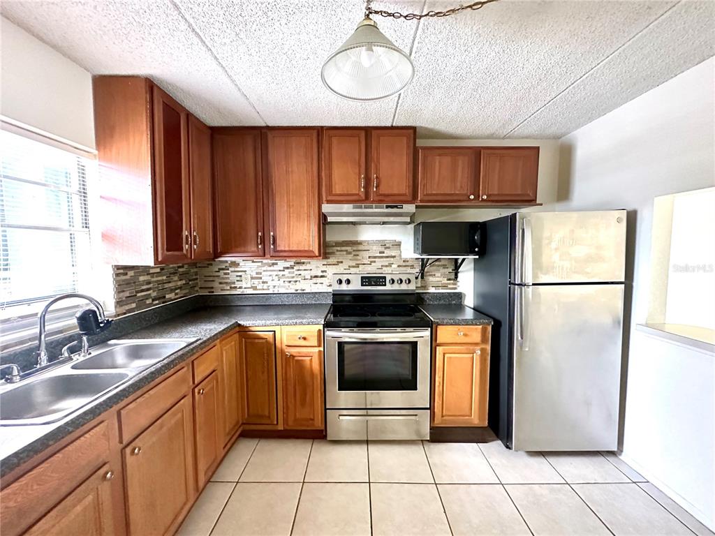 A kitchen features wooden cabinets, stainless steel appliances, a tiled backsplash, and light floor tiles — 2830 SOMERSET PARK DRIVE UNIT 201, TAMPA, FL