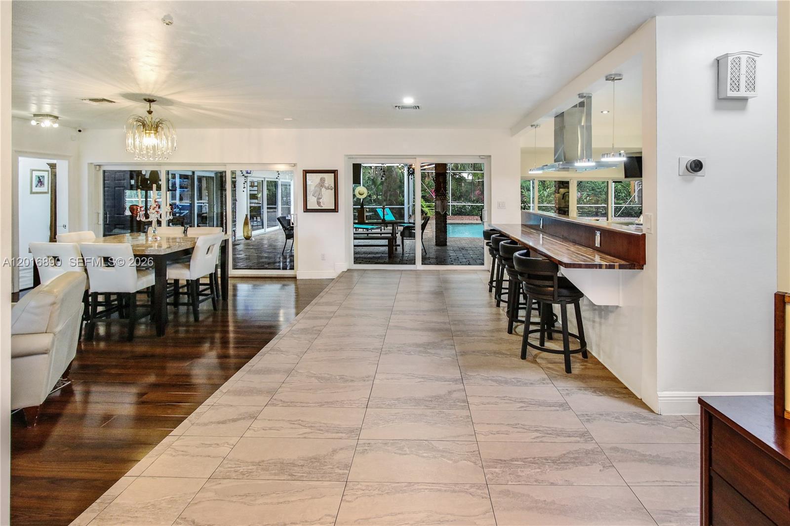 A dining area with hardwood floors transitions to a tiled kitchen bar and patio view — 19901 NE 21st Ave, Miami FL 33179, MIAMI, FL