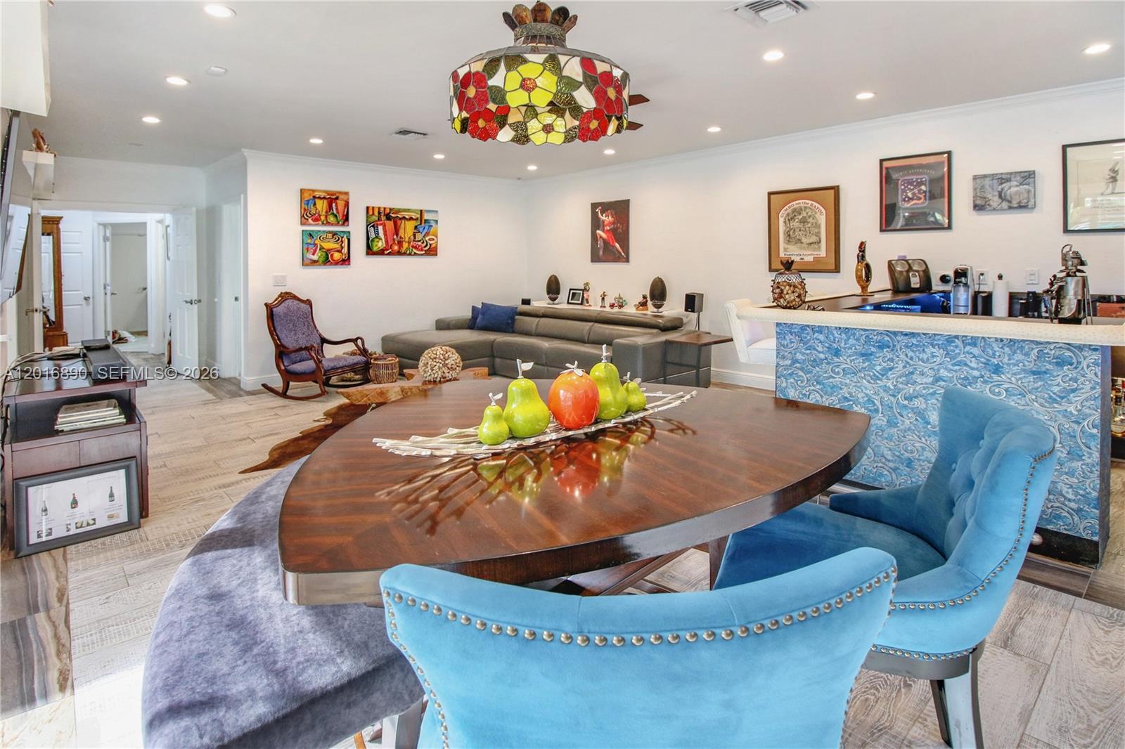 A dining area with a triangular table and blue chairs overlooks a living room space — 19901 NE 21st Ave, Miami FL 33179, MIAMI, FL
