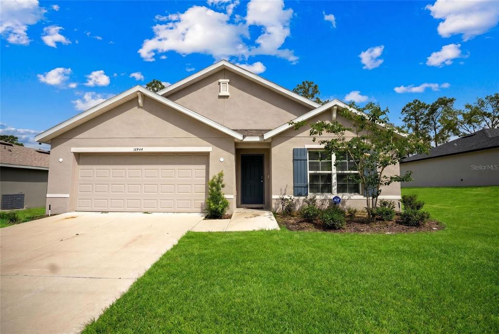 A single-story suburban house with a beige stucco exterior, a two-car garage, and blue shutters — 14944 SW 66TH AVENUE ROAD, OCALA, FL