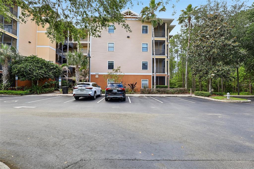 A multi-story apartment building with a parking lot and two parked cars in front — 9055 TREASURE TROVE LANE UNIT 208, KISSIMMEE, FL
